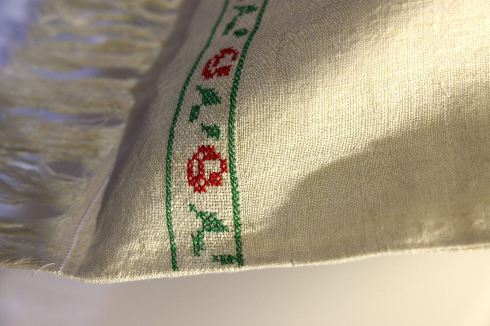 Fascia di rose rosse e foglie verdi ricamate a punto croce su un telo di lino con le frange, nella luce del pomeriggio